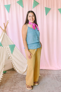 woman wearing golden yellow wide-leg pants with a blue button-front cami top and pink bandana scarf, styled with platform sandals