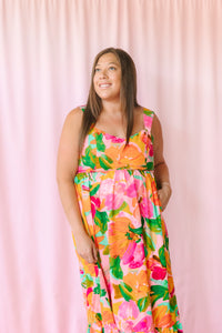 Close-up of model in bold floral maxi dress with painterly orange and hot pink flowers and square neckline