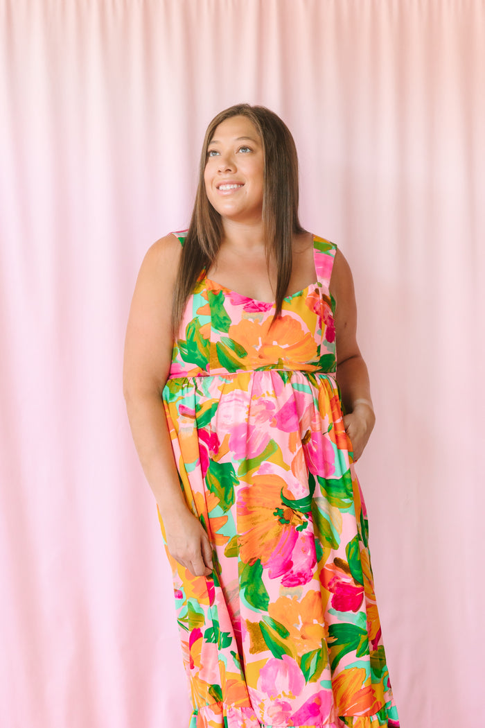 Close-up of model in bold floral maxi dress with painterly orange and hot pink flowers and square neckline