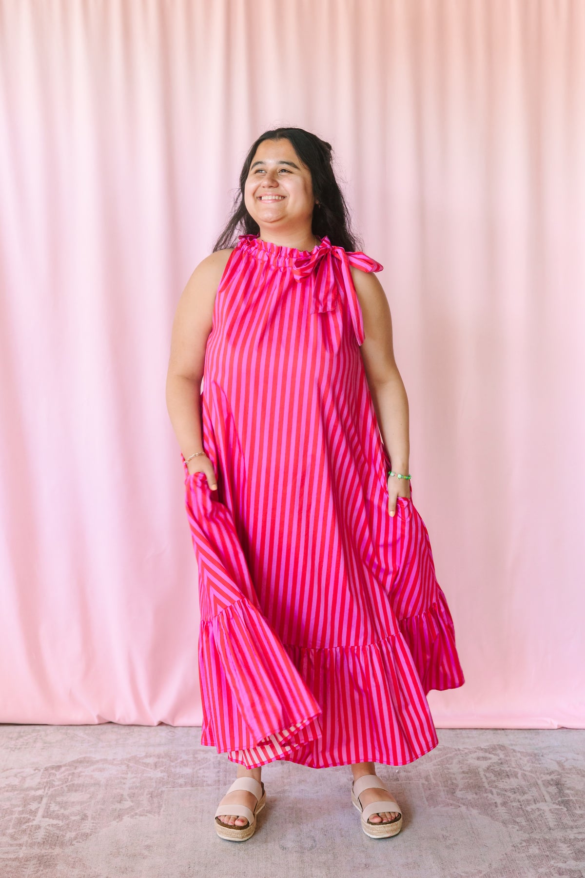 Woman wearing a bold pink and red striped maxi dress with tiered ruffle hem, styled with platform sandals
