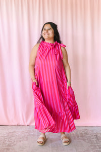 Woman wearing a bold pink and red striped maxi dress with tiered ruffle hem, styled with platform sandals