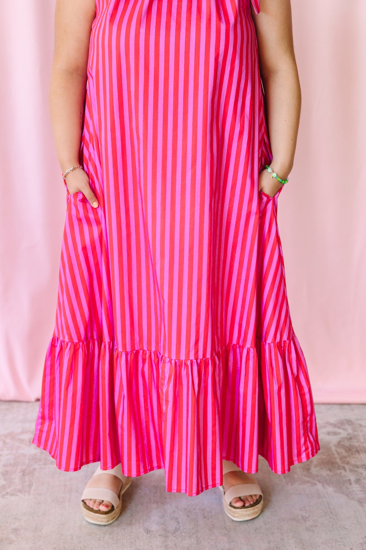 Detail shot of tiered ruffle hem on a hot pink and red striped maxi dress with side pockets, worn with platform sandals