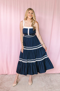 Woman wearing navy and white tiered maxi dress with square neckline, white contrast straps, and button-front bodice detail, styled with nude heels