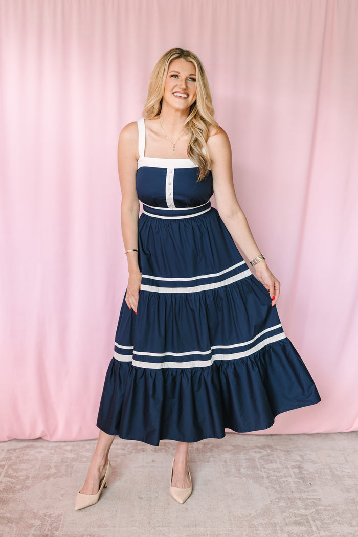 Woman wearing navy and white tiered maxi dress with square neckline, white contrast straps, and button-front bodice detail, styled with nude heels
