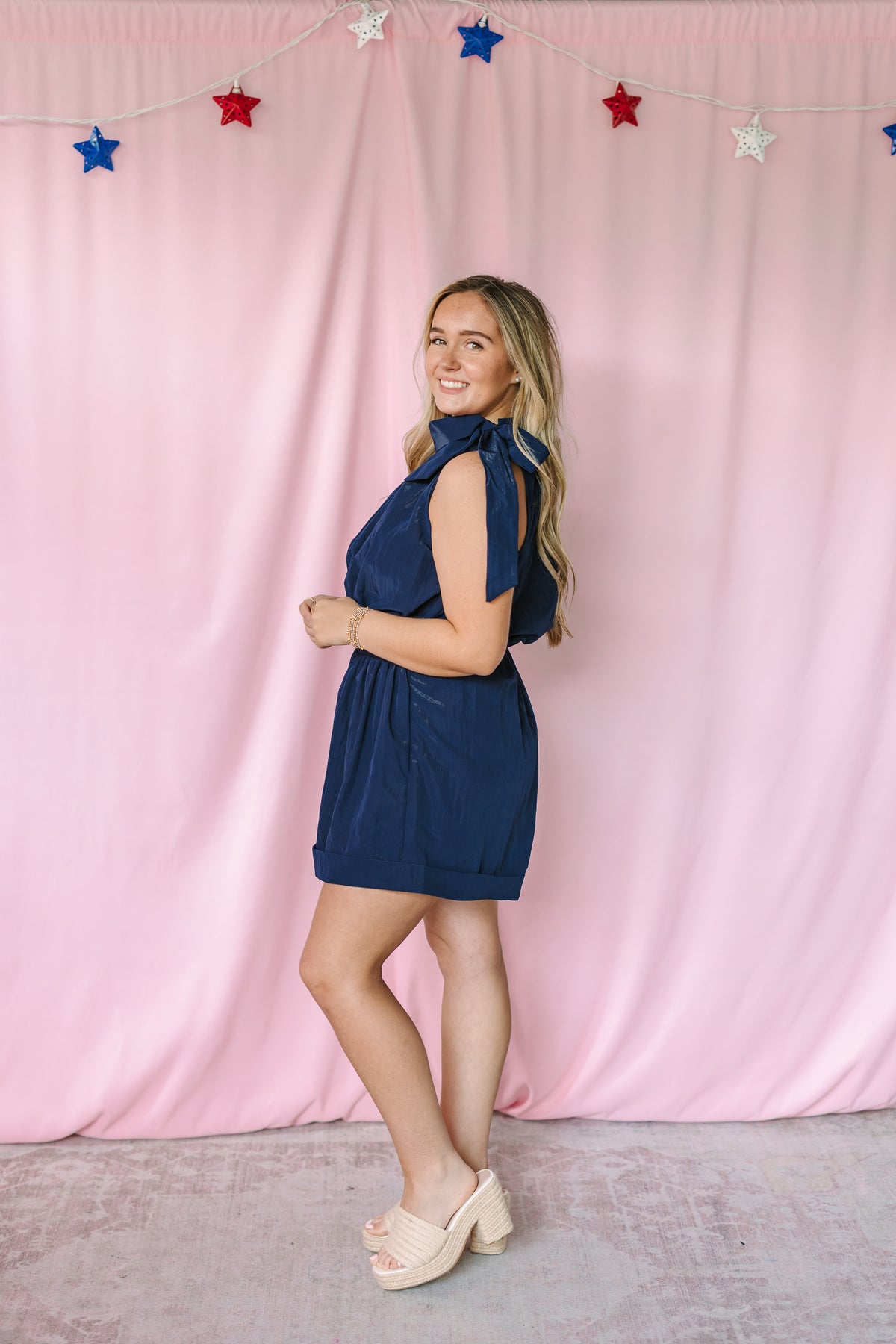 Navy sleeveless romper with bow tie halter neckline and elasticized waist – side view on model