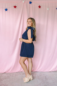 Navy sleeveless romper with bow tie halter neckline and elasticized waist – side view on model